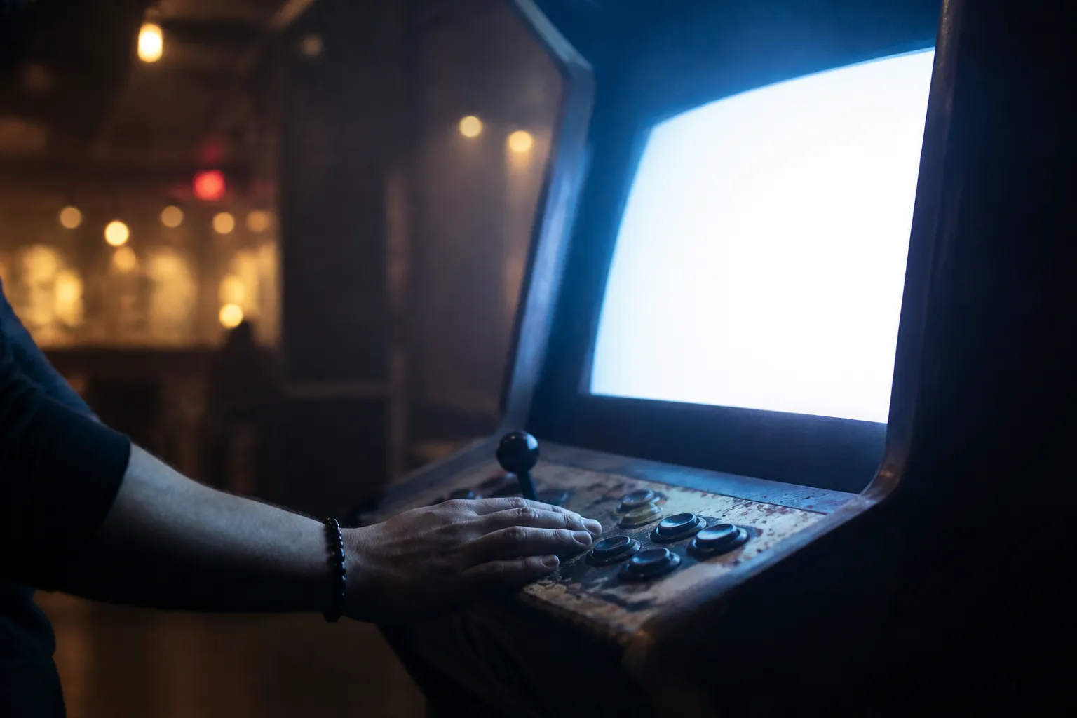 A glowing arcade cabinet in a dim room springs back to life as a hand rests on the joystick, ready for the next attempt.