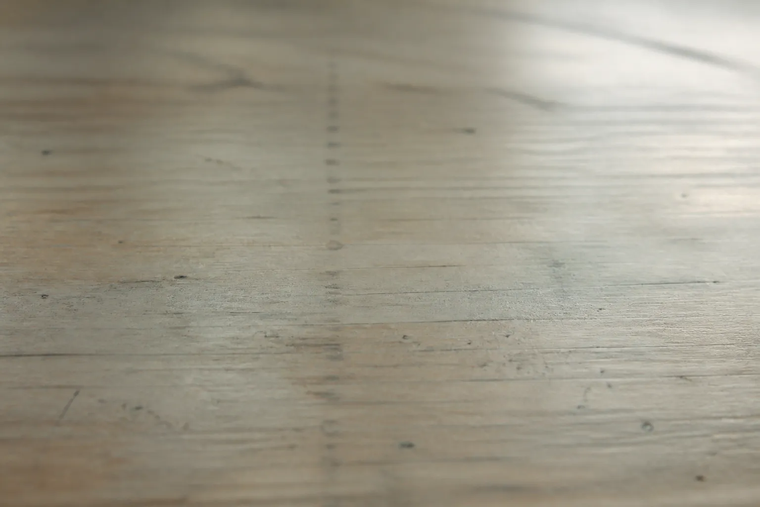 Illustrative image: a soft, unfocused view of a worn classroom desk in muted sage and oak tones, with faint pencil marks and gentle window light.